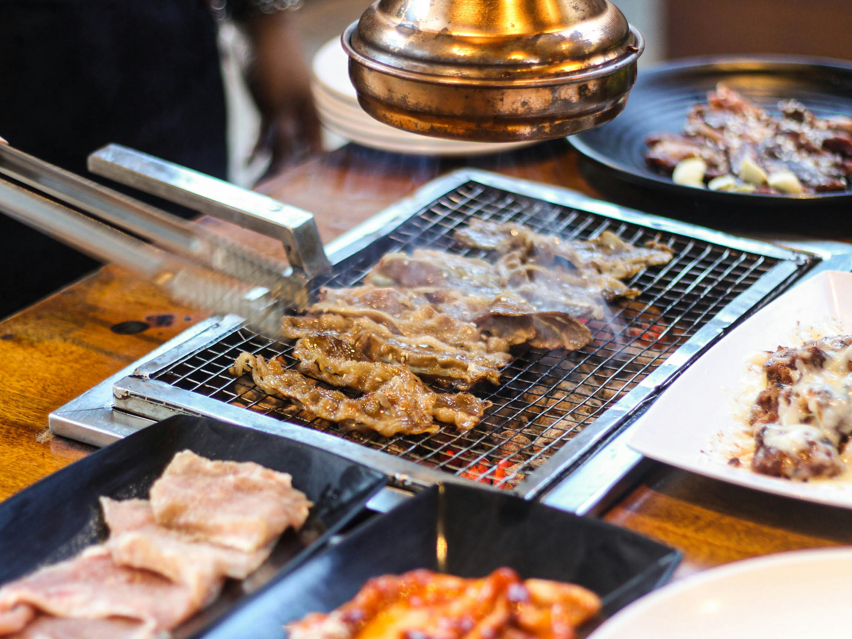 Grilled Samgyeopsal pork belly slices sizzling on a Korean BBQ grill with fresh lettuce and garlic on the side